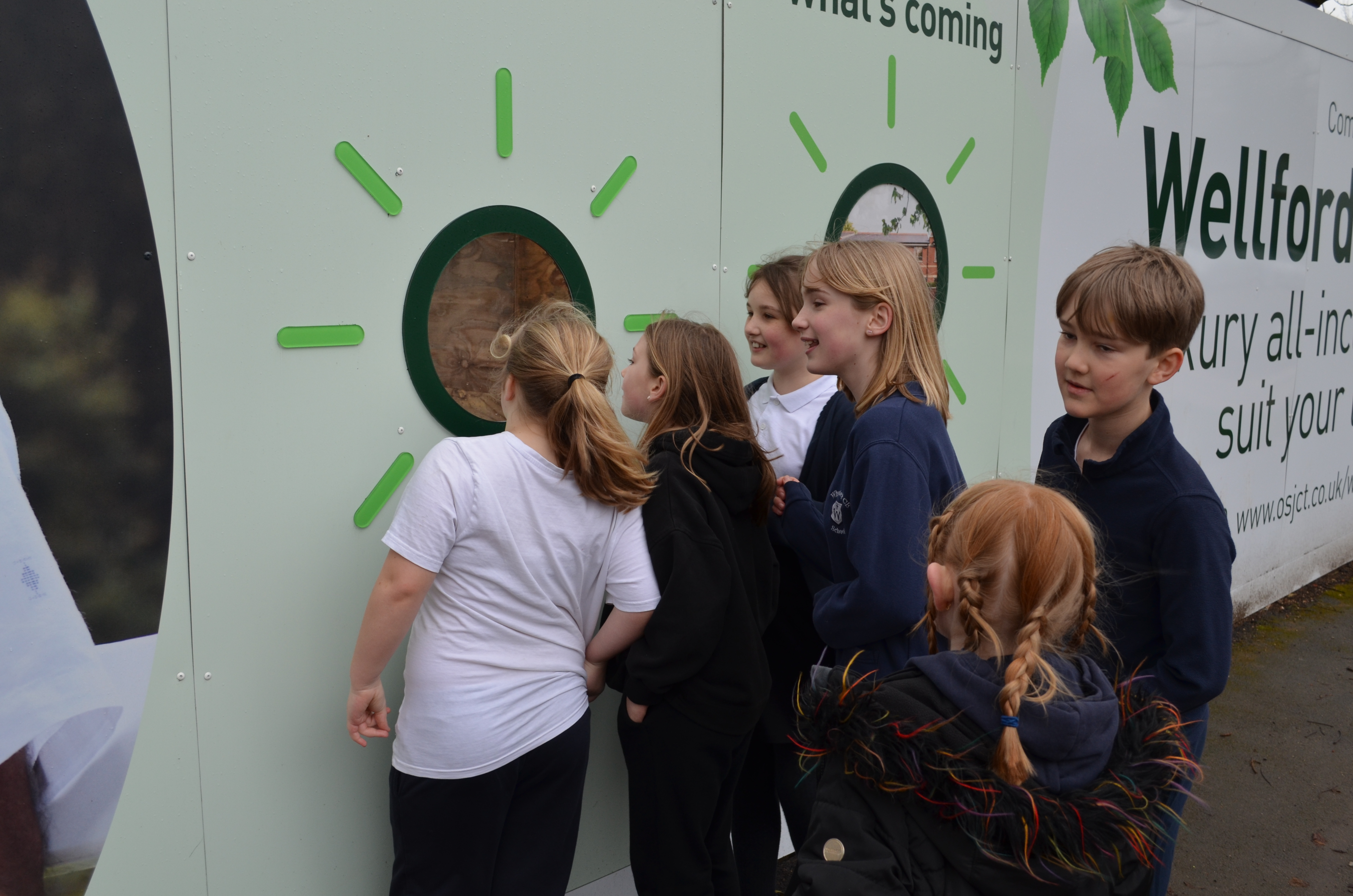 school children looking through a peek hole at the building site
