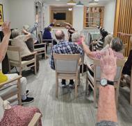 Edwardstow Court residents take part in a seated mobility exercise session, raising their arms together to improve strength and flexibility.