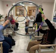 Residents at Edwardstow Court participate in a group mobility activity using exercise hoops to support movement, coordination and upper body strength.
