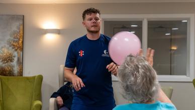 Cricket coach leads a seated balloon game with care home residents.