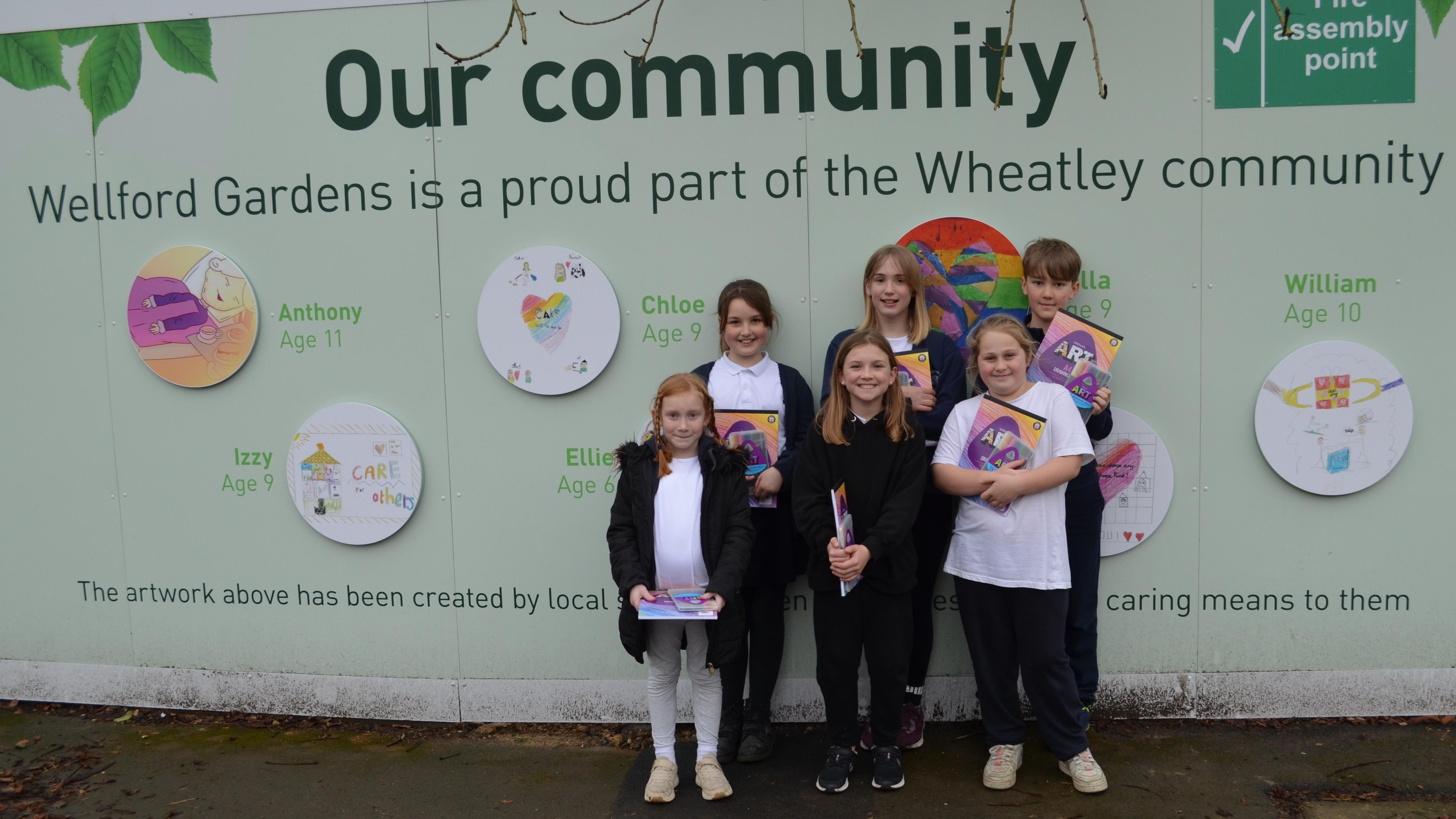Children from Wheatley Primary School standing in front of their artwork on hoarding at the building site