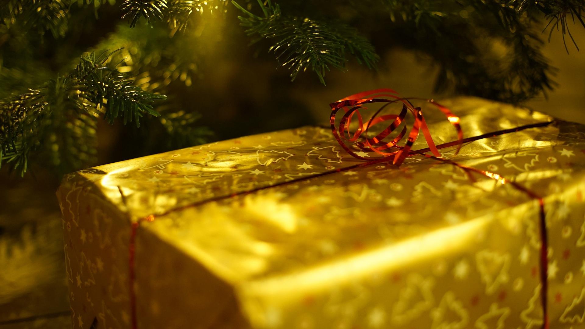 A Christmas gift wrapped in gold paper beneath a Christmas tree