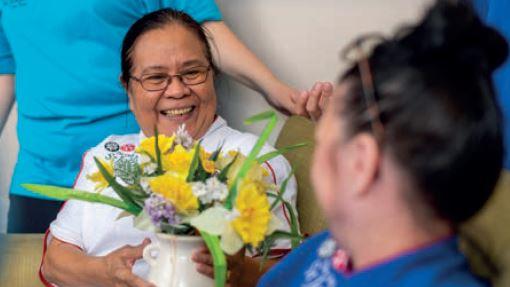 A nurse holds flowers, talking to a carer