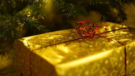 A Christmas gift wrapped in gold paper beneath a Christmas tree
