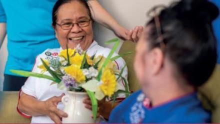 A nurse holds flowers, talking to a carer